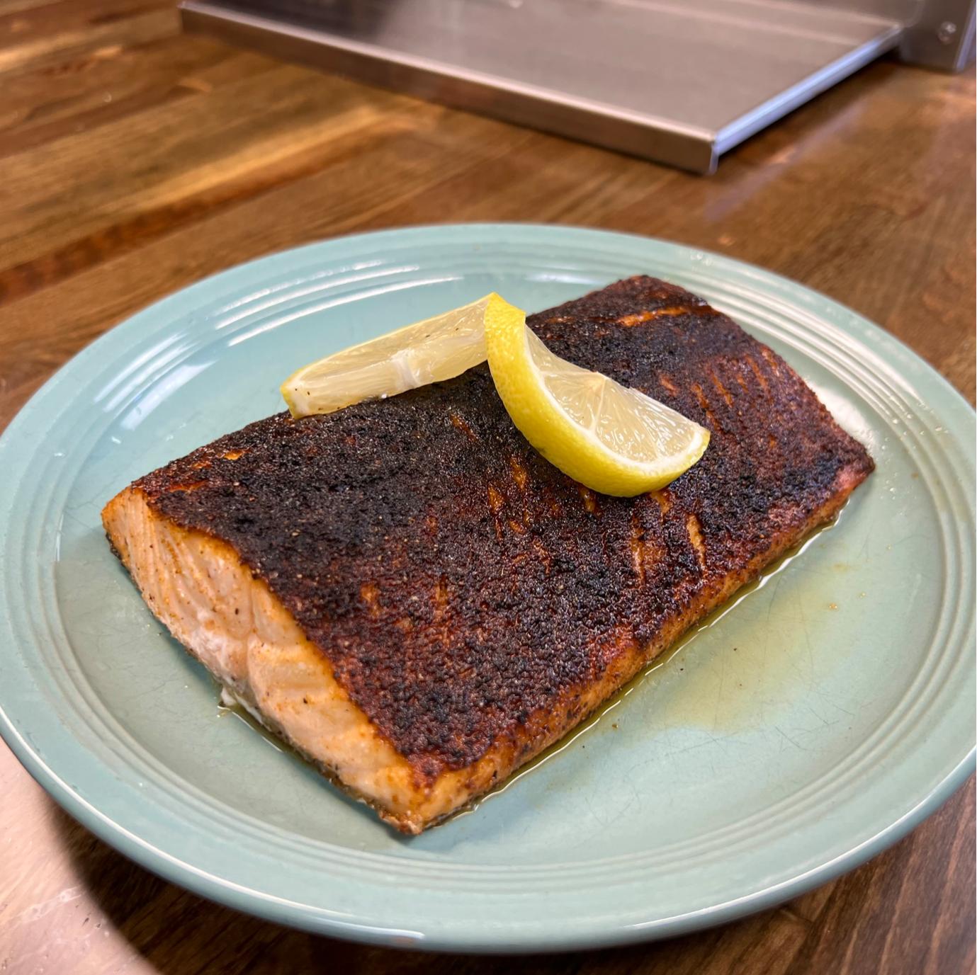 Grilled blackened salmon fillet with lemon wedges on a blue plate