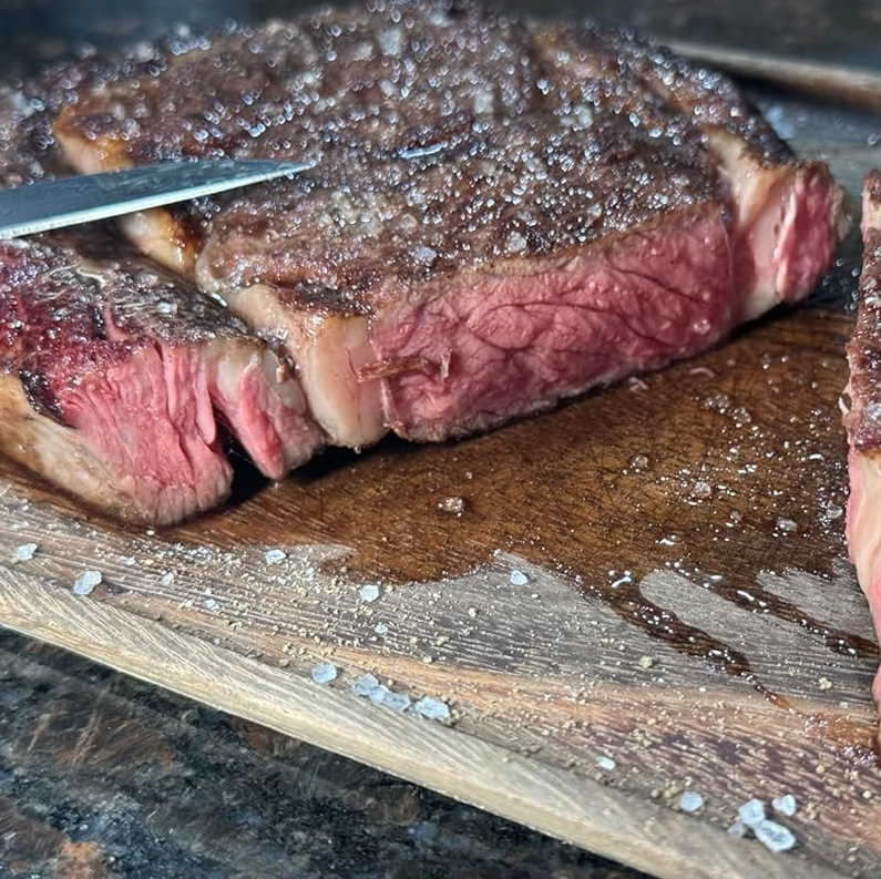 The stainless steel BIGHORN oven with its door open, sitting on an outdoor table next to a board of sliced salami.