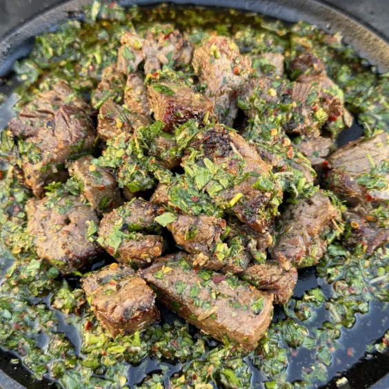 Grilled steak bites covered with green chimichurri sauce in a skillet