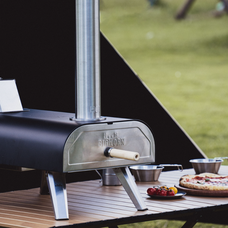 Outdoor pizza oven beside a prepared pizza on a garden table