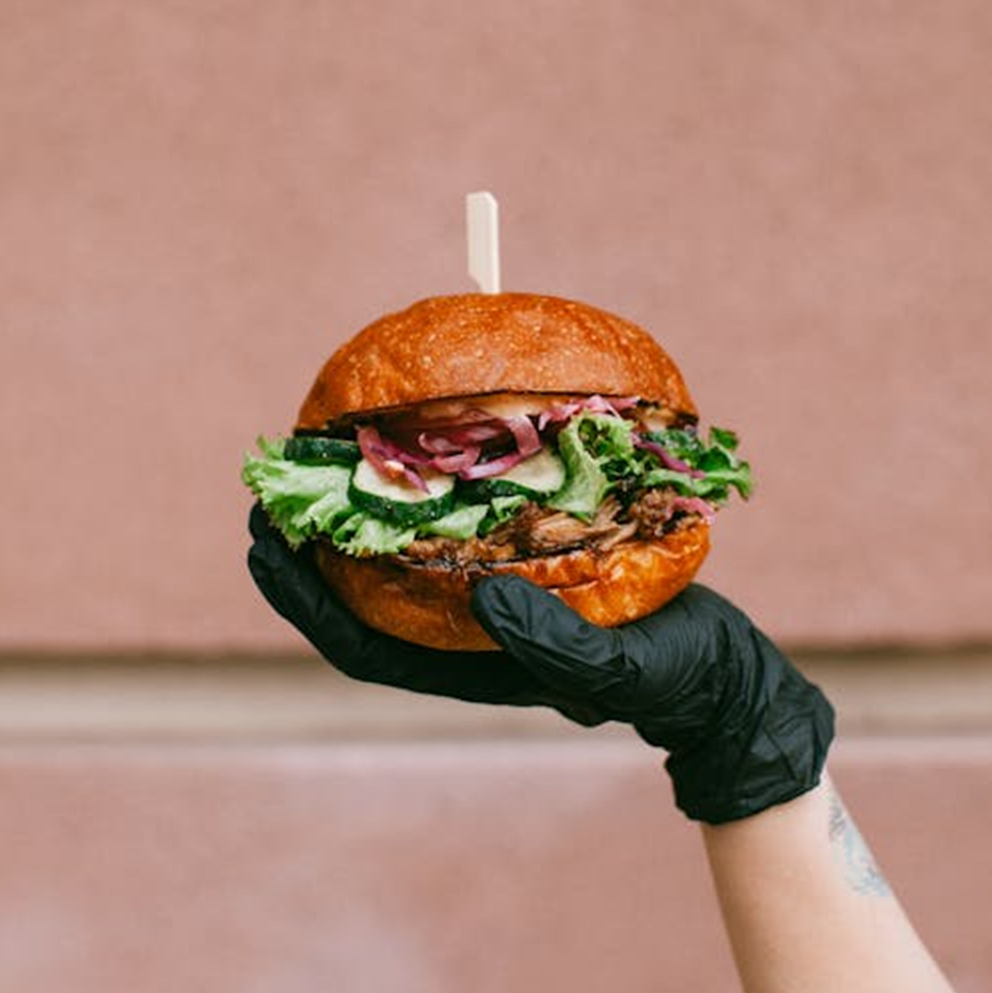 A hand in a black glove holding a gourmet burger.
