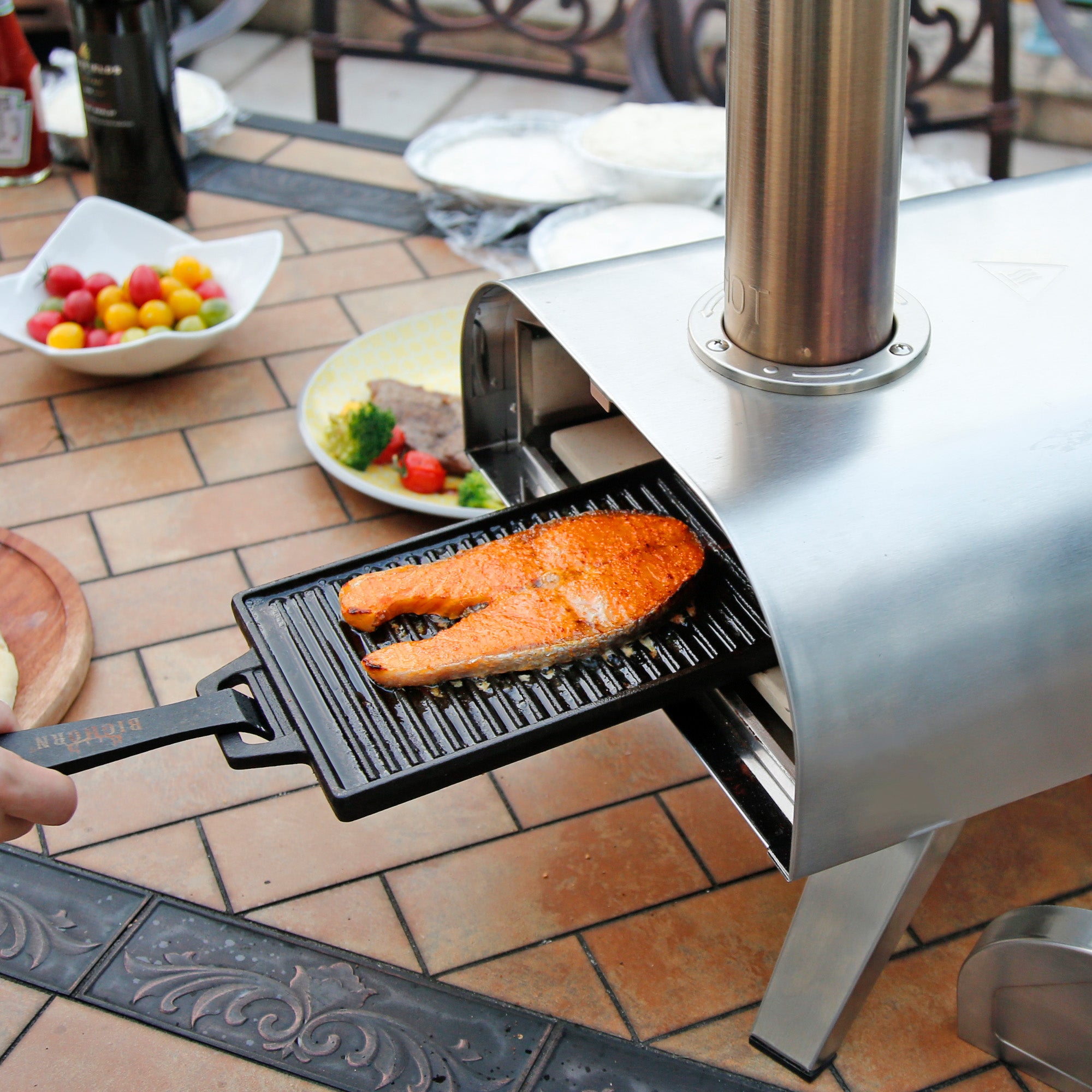 Stainless steel Big Horn Outdoors pizza oven grilling salmon fillet on a black griddle for outdoor cooking.