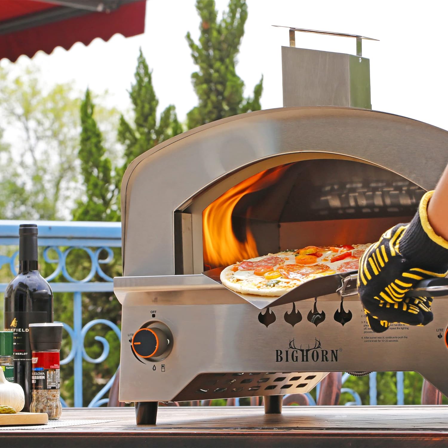 BIGHORN 13 inch stainless steel gas pizza oven baking pizza outdoors, with a pizza being placed inside.