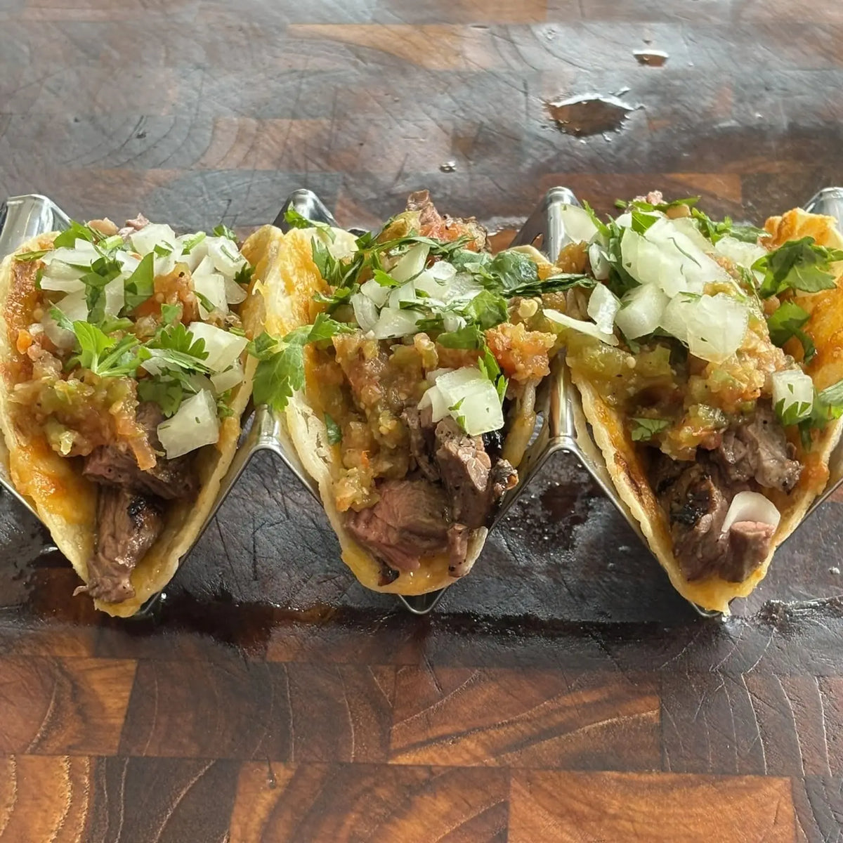 Three steak tacos topped with diced onion and chopped herbs