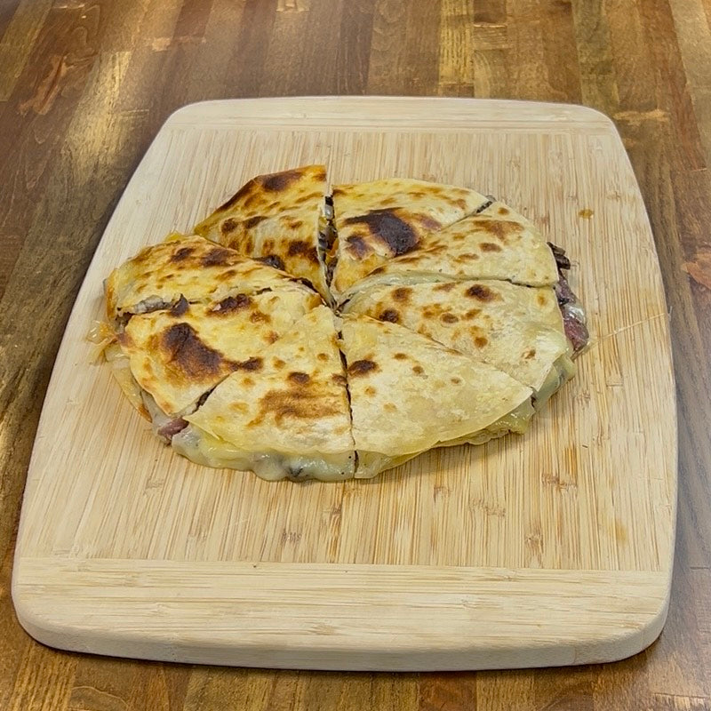 Sliced steak and cheese quesadilla on a wooden cutting board.