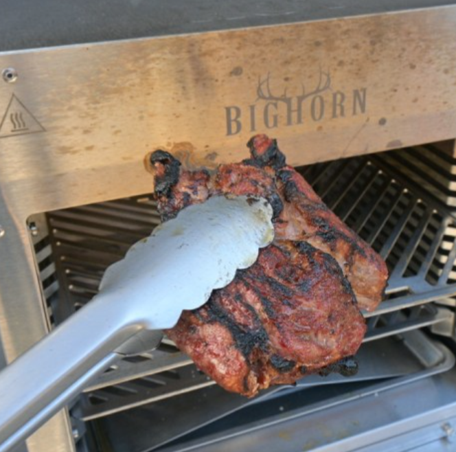 Grilled steak held with tongs in front of Bighorn infrared grill