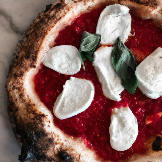 A close-up of a cooked Neapolitan pizza with a charred crust, tomato sauce, and fresh mozzarella.