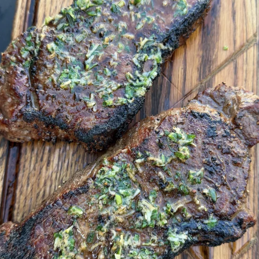 Sliced grilled strip steaks topped with melted garlic herb butter on wooden board