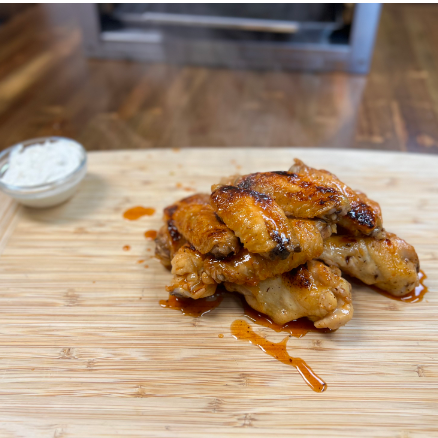 Sweet and spicy grilled chicken wings stacked on a wooden cutting board