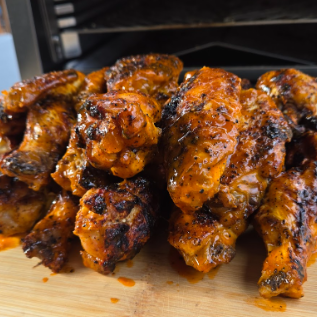 Close-up of a stack of glazed, grilled chicken wings on a wooden cutting board.