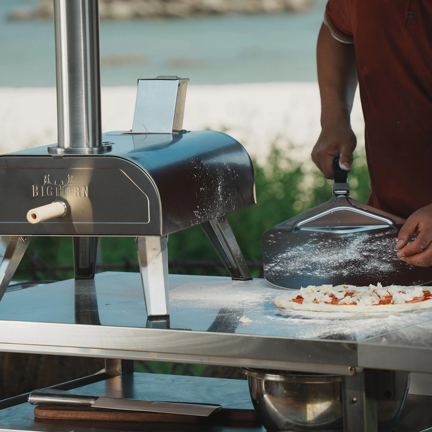 Outdoor pizza oven with cook preparing pizza dough on stainless steel table