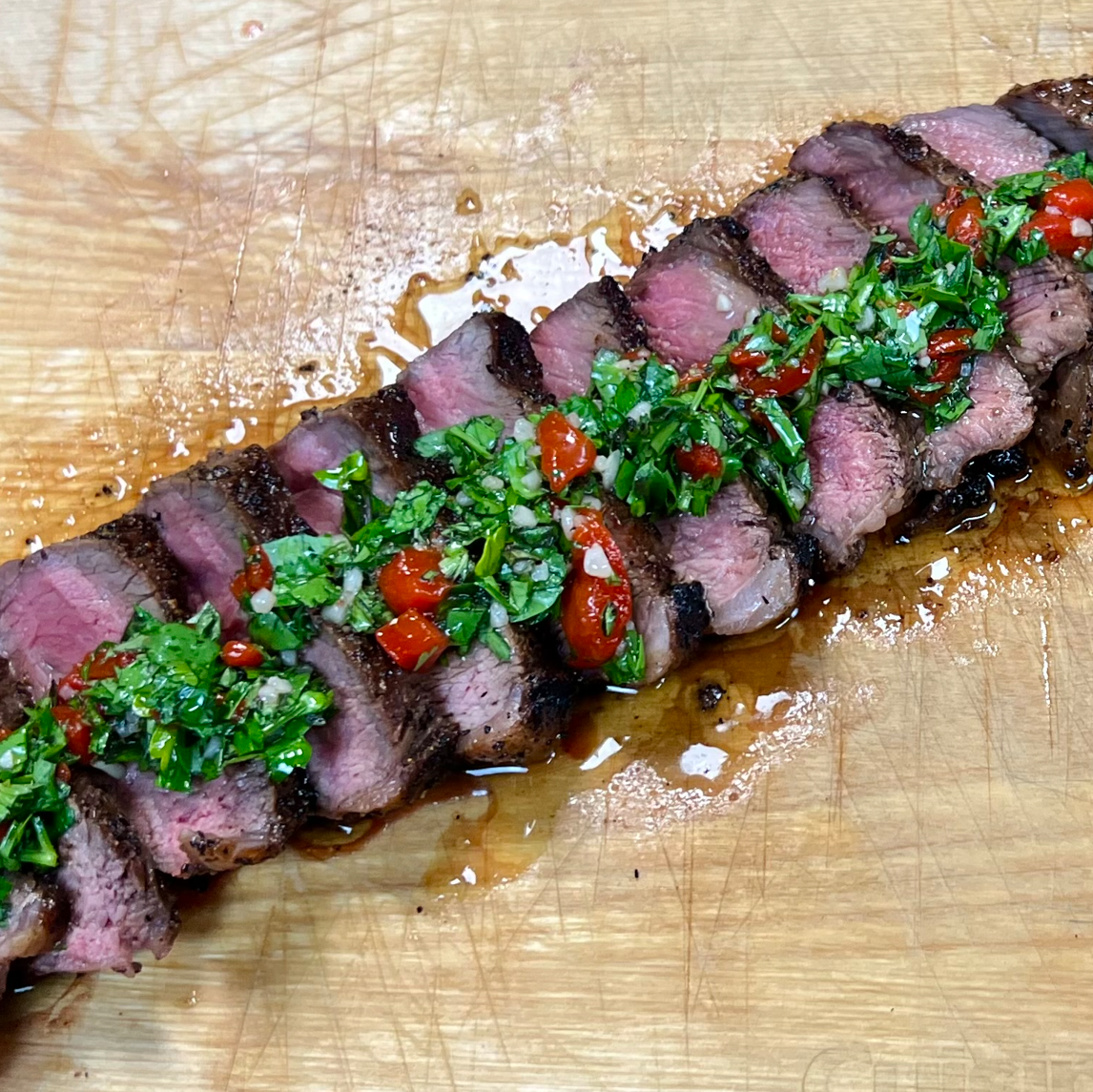 Close-up of sliced picanha steak topped with fresh green and red chimichurri sauce.