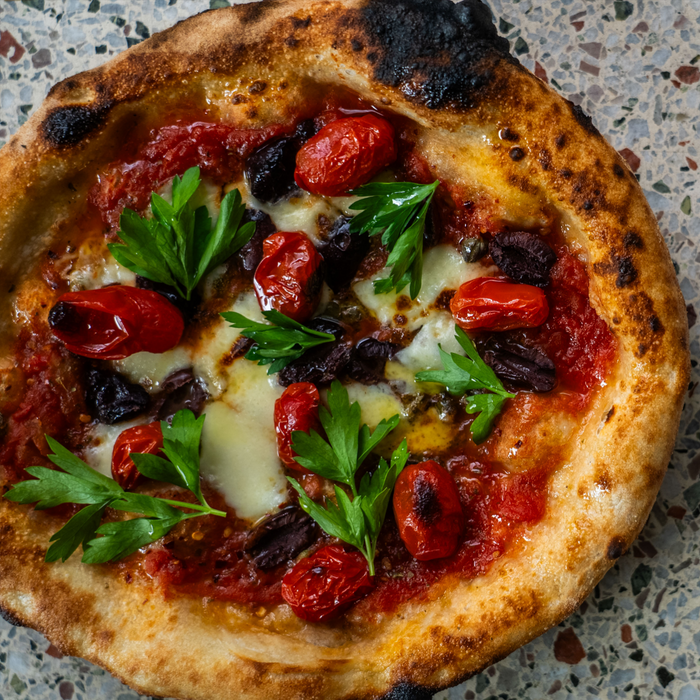 A freshly baked Neapolitan pizza with a puffy, charred crust, topped with roasted tomatoes and fresh parsley.
