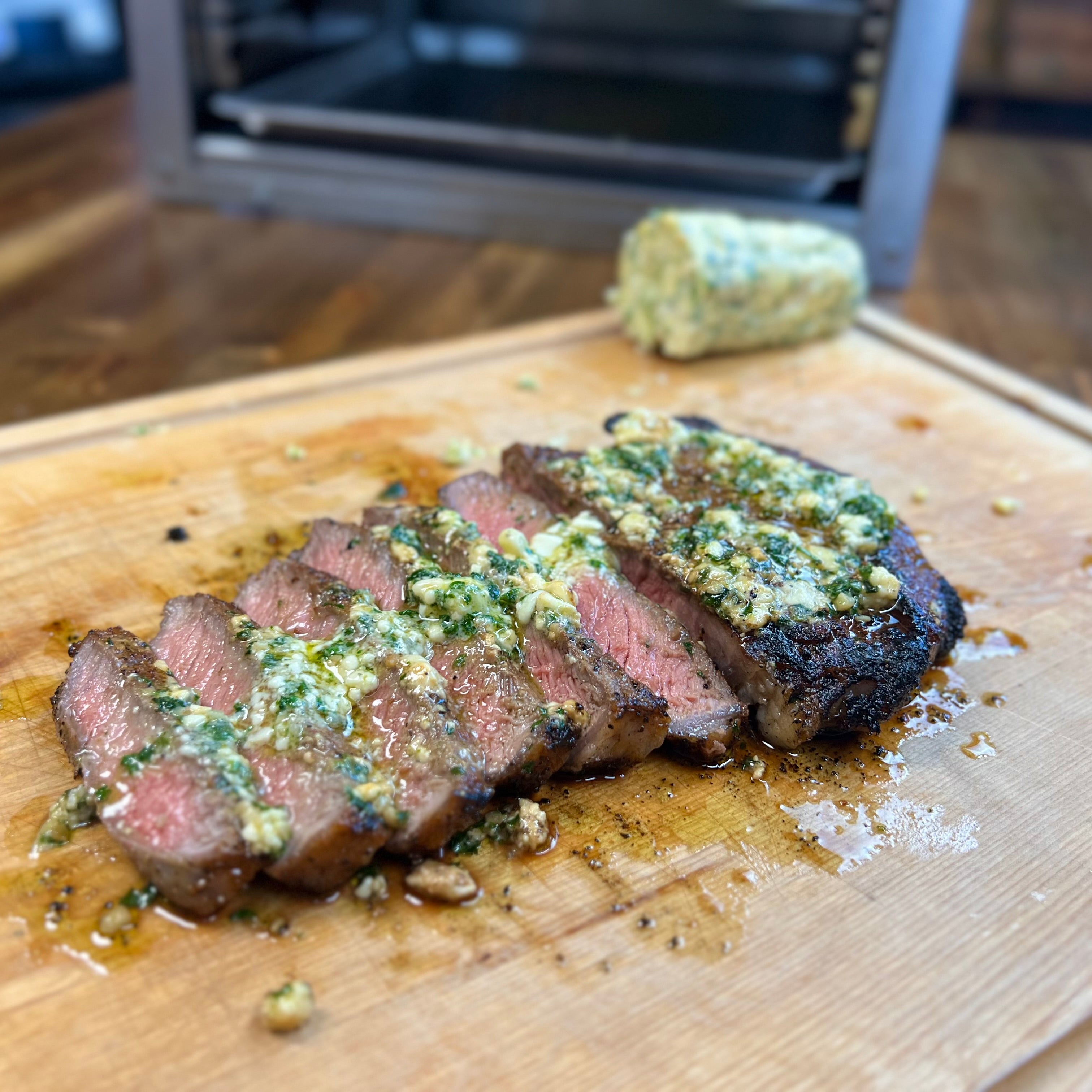 Sliced medium-rare steak topped with garlic herb butter on a wooden cutting board
