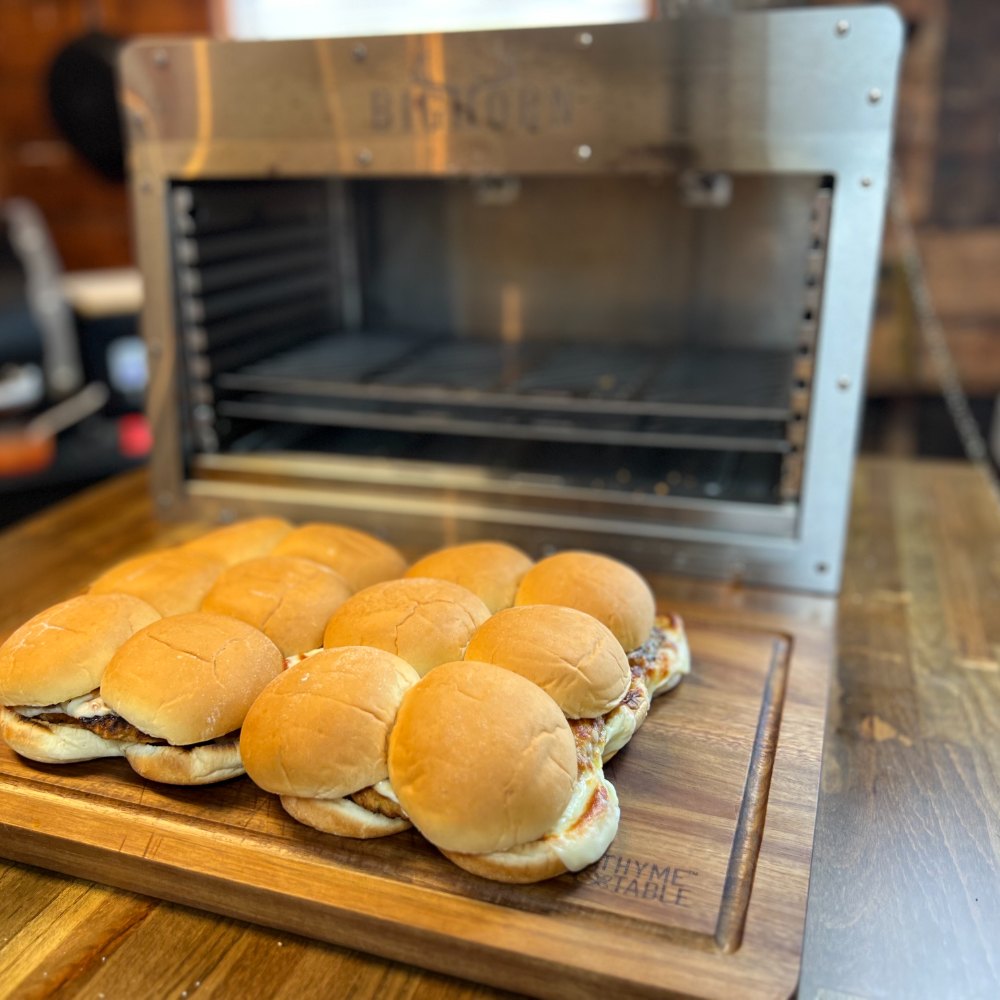 Cheesy slider sandwiches on a wooden board in front of a Big Horn pizza oven