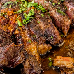 Close-up of a perfectly seared, thick-cut steak sliced and resting in juices with fresh herbs
